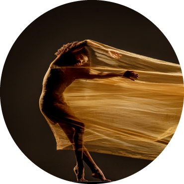 Dancer wears gold clothing and is captured in motion in front of a black backdrop