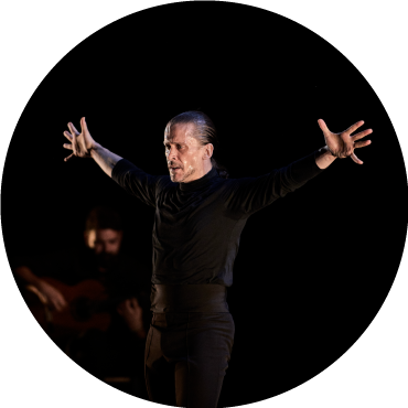Dancer is captured in motion with his arms spread out, wearing black against a black backdrop