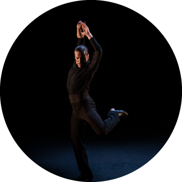 Dancer is captured in motion wearing black against a black backdrop