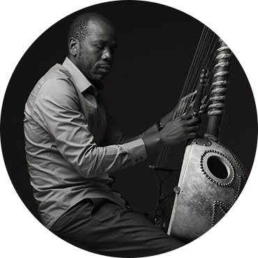 Ballaké Sissoko holds his kora and poses against a black backdrop