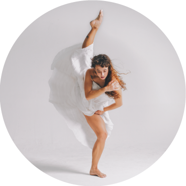 A member of Body Traffic wears a white dress and is pictured balancing on one leg against a white backdrop