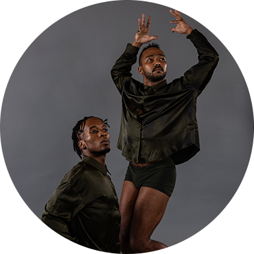 Two dancers are captured in movement wearing black clothing against a gray backdrop