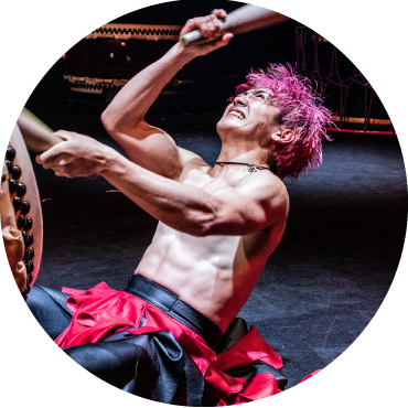 Drummer captured performing live with his arms in motion as he looks upward with pink colored hair