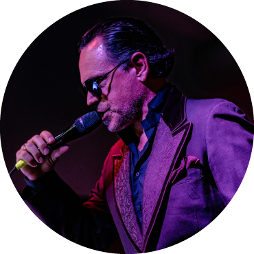 Portrait view of Kurt Elling singing into a microphone, wearing a suit and dark sunglasses