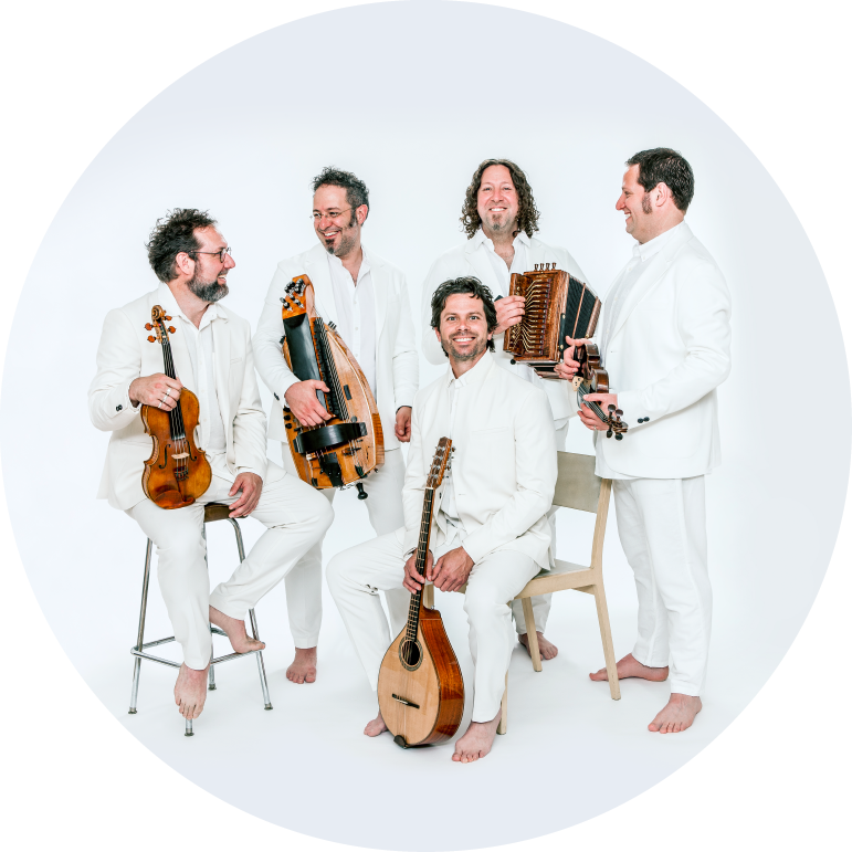 The band members wear white suits and hold their instruments standing in front of a white backdrop