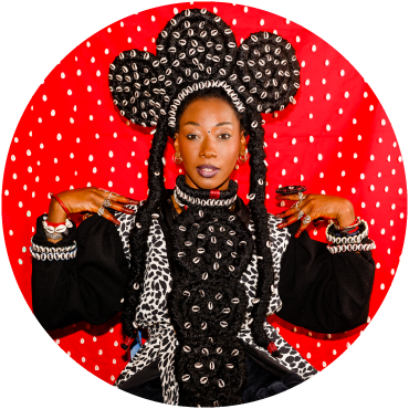 Fatoumata wears a black outfit and poses against a red backdrop with her hands on her shoulders