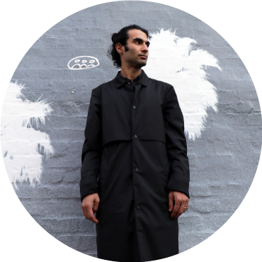Tigran Hamasyan wears black clothing and looks off to the side against a gray and white backdrop